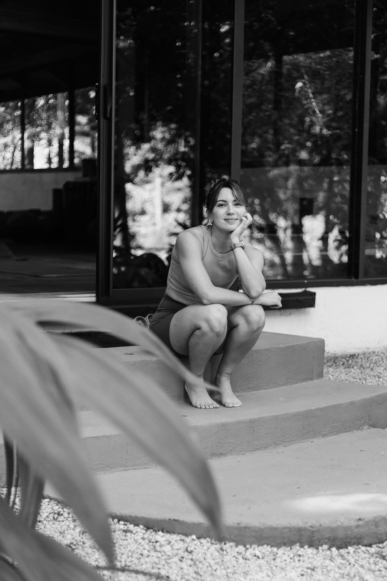Black-and-white portrait of Sofía Ballard crouching on the studio steps, smiling.